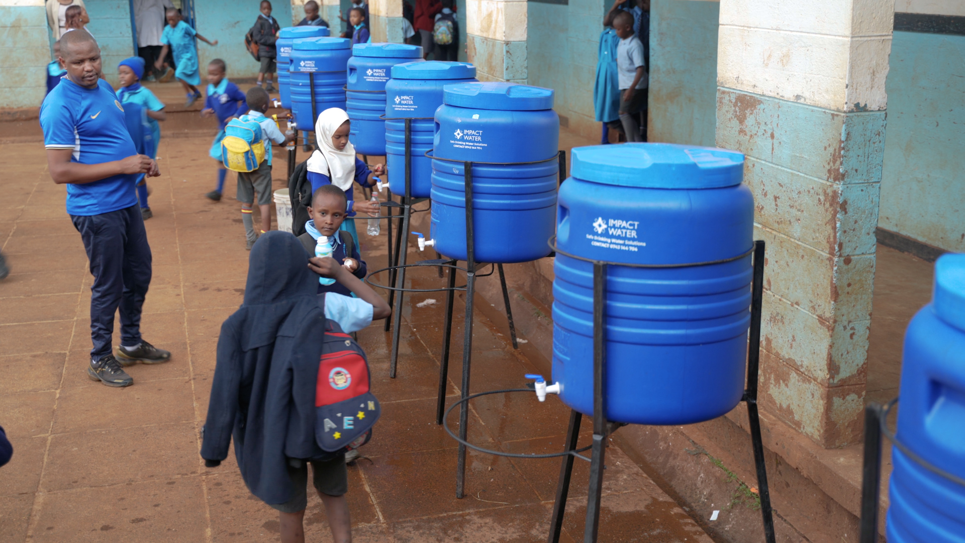 Students in Kenya lining up to use large blue water stations, demonstrating the impact of a safe water access program in a school.