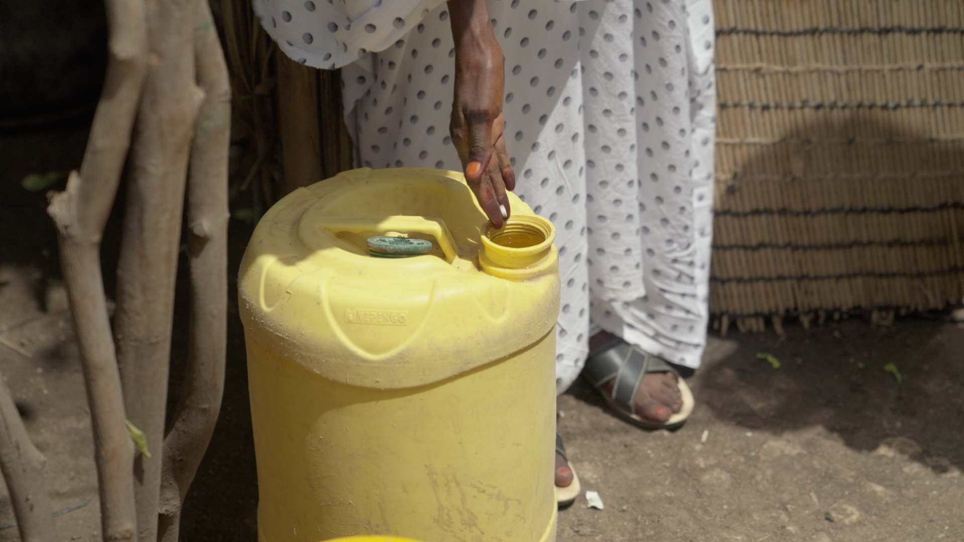 Person adding water purification drops to a jerrycan, symbolizing water treatment in communities.