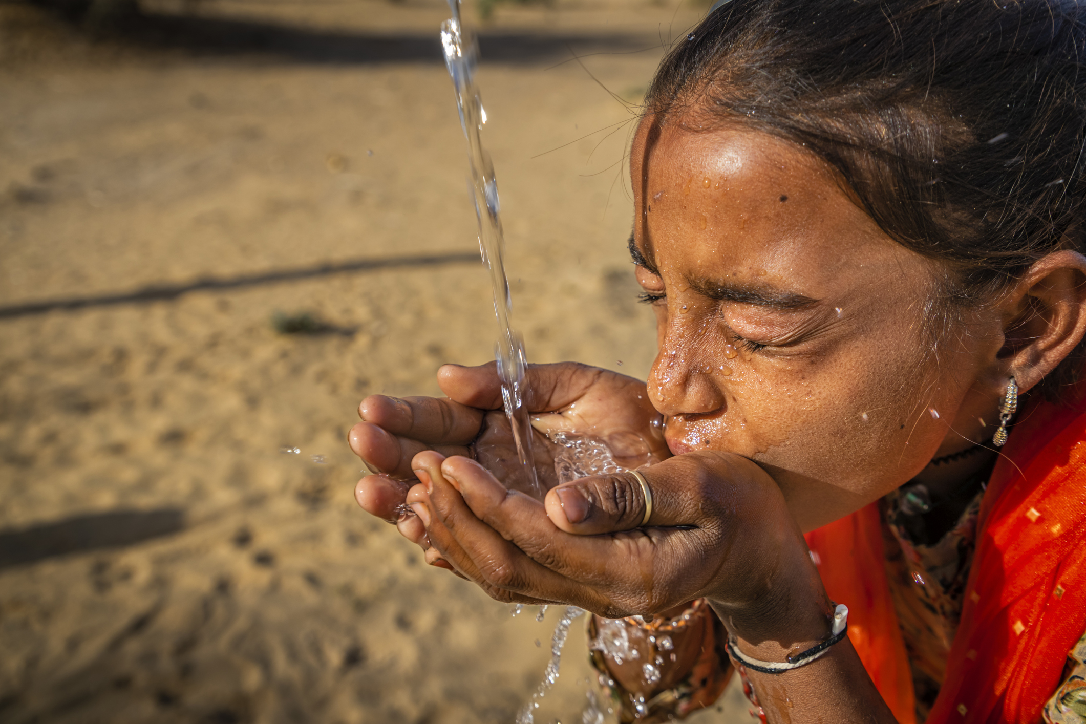 Young person drinking clean water from cupped hands, highlighting the fundamental human need for safe hydration.