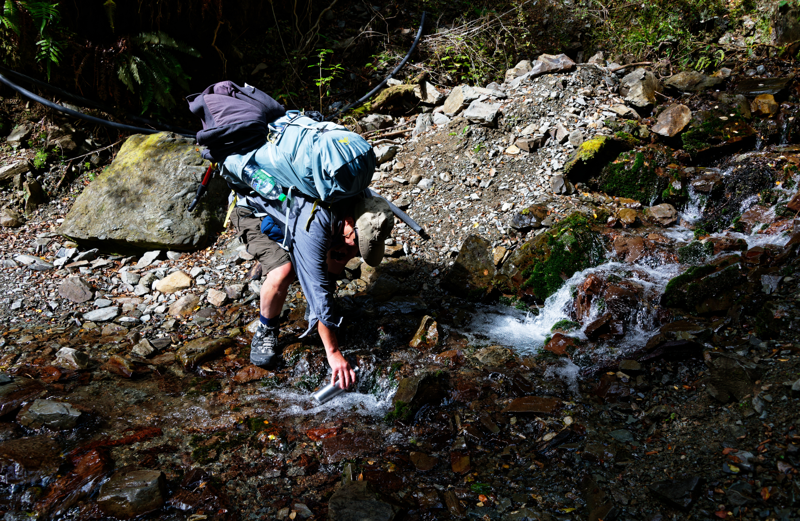 A stainless steel drinking bottle is being refilled with fresh water from a river