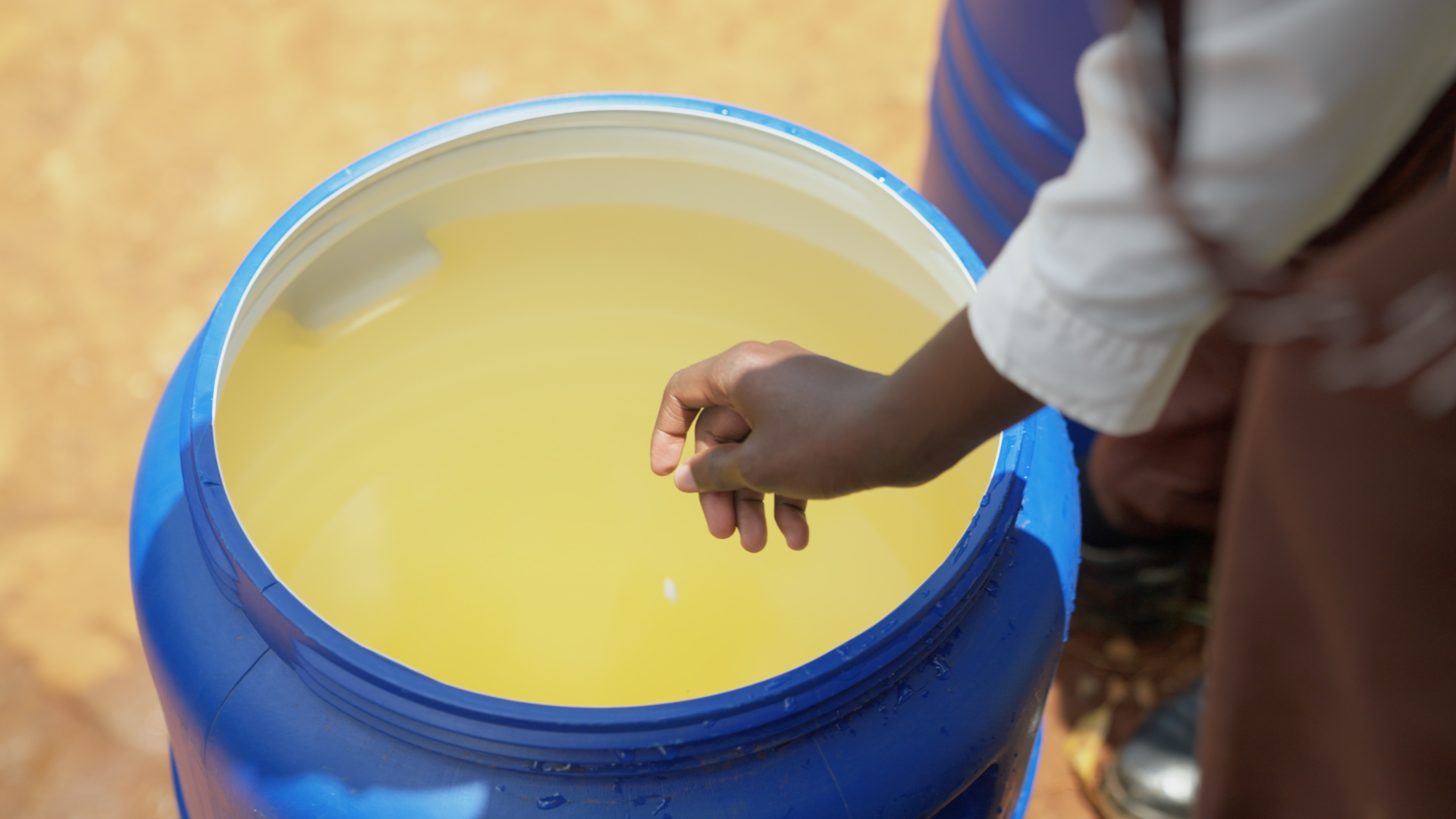 A person dropping an Aquatabs tablet into a large container of water, demonstrating point-of-use water disinfection.